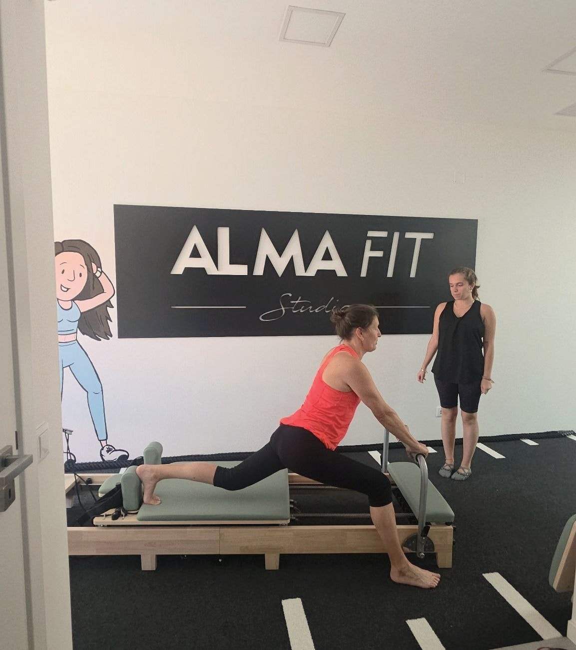 Aula de Pilates Reformer: uma aluna faz um exercício na máquina acompanhada pela instrutora.