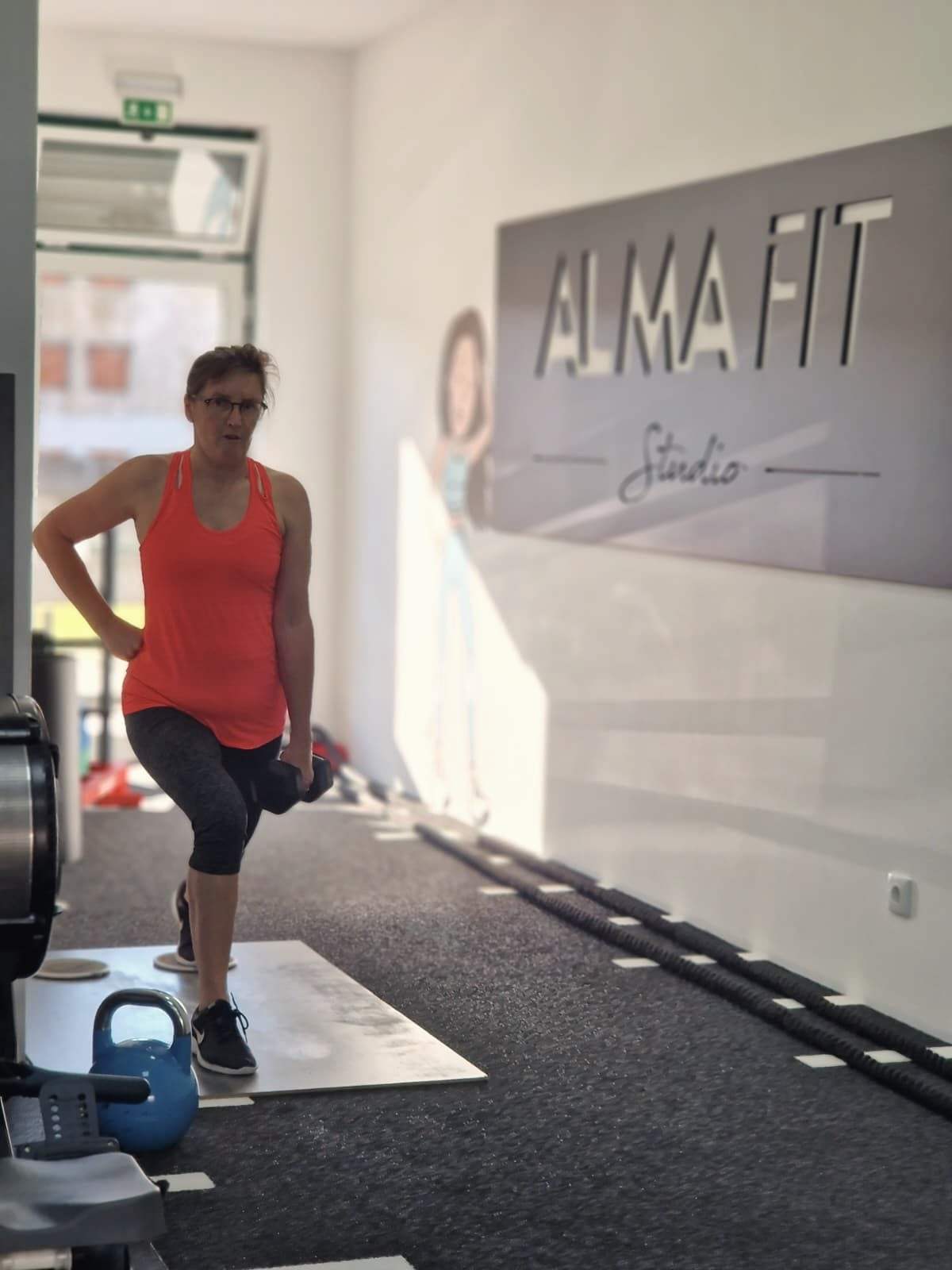 Aluna a fazer uma afundo com kettlebell no estúdio.